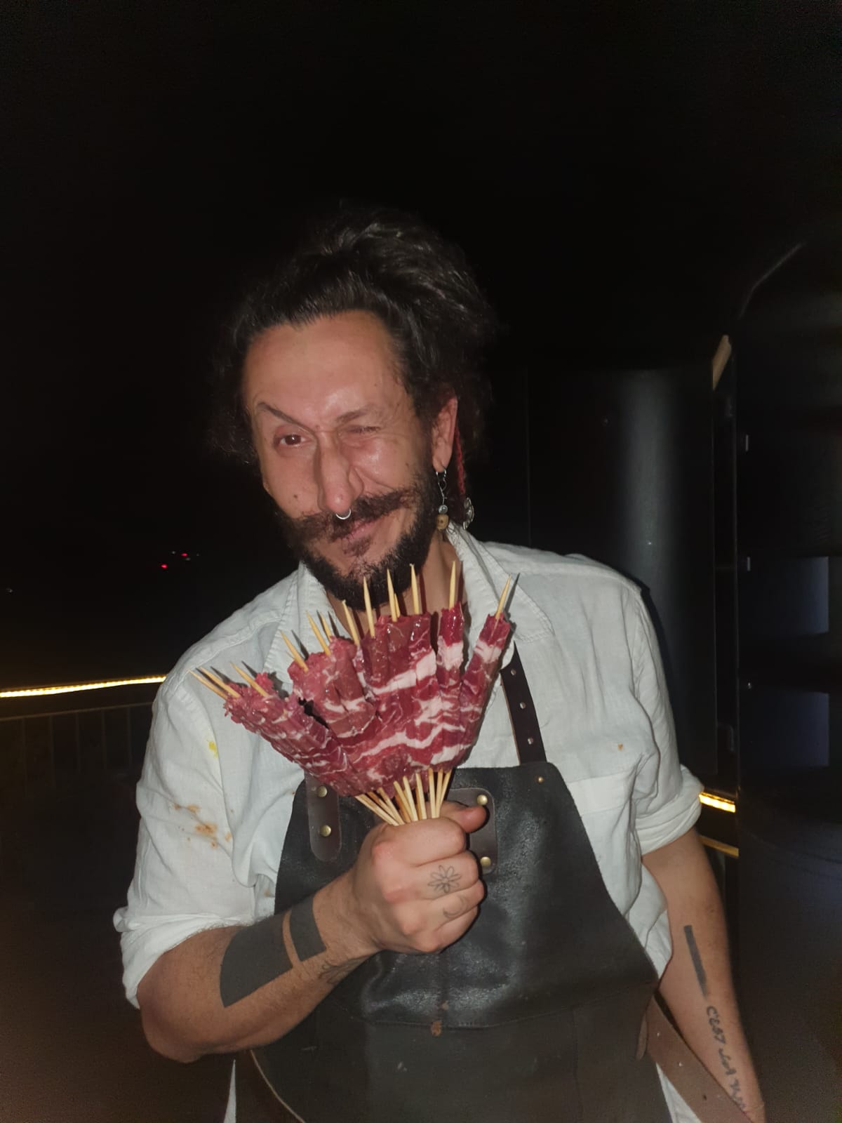 Chefkoch Marco Belotti zwinkert und hält Fleischspieße
